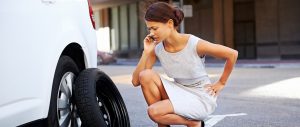 Unknown person talking on phone while kneeling down to tire problem on vehicle